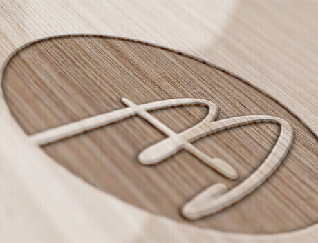 Close-up of a wooden surface featuring an engraved oval shape with a stylized letter "A" inside it, crafted by a leading brand design agency in Toronto. Conte Studios