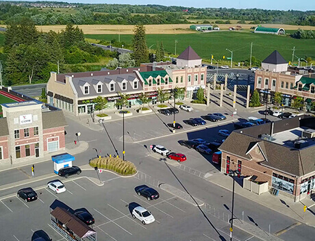 Aerial view of a small shopping center with parked cars, surrounded by green fields and trees, resembling the harmonious design crafted by a top web design agency in Toronto. Conte Studios