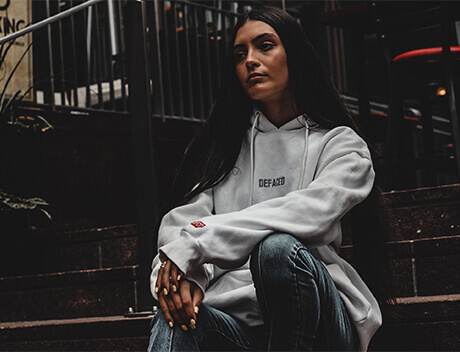 A person sitting on steps in a white hoodie and jeans, their long dark hair flowing freely, exudes a casual vibe. The scene captures the laid-back yet creative essence akin to that of Conte Studios, a renowned web design agency based in Toronto. Conte Studios