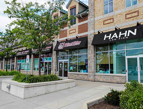 A row of storefronts, including HAHN and Conte Studios, with large windows and striped awnings. The area features trees, planters, and a sidewalk in front. Conte Studios