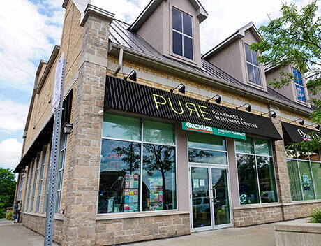 Street view of "PURE Pharmacy & Clinic" with a glass entrance, brick exterior, and surrounding greenery, reflecting the modern and innovative spirit typical of a top Toronto Design Agency. Conte Studios