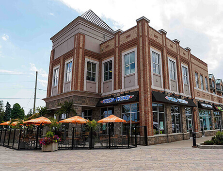 Two-story brick restaurant with large windows, outdoor seating area featuring orange umbrellas, and a "Wild Wing" sign on the front. Designed by Conte Studios, a leading content creation agency in Toronto. Conte Studios