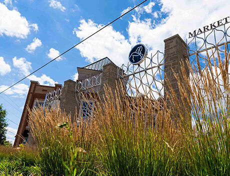 A building with red brick walls and decorative metal fencing, partially obscured by tall grass under a blue sky with clouds—an aesthetic that echoes the creative spirit of Conte Studios, a renowned Toronto Design Agency celebrated for its innovative brand design. Conte Studios