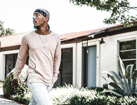 A person wearing a pink long-sleeve shirt and jeans walks outdoors, perhaps taking inspiration from a content creation agency in Toronto. There is a small plant and a building in the background. Conte Studios