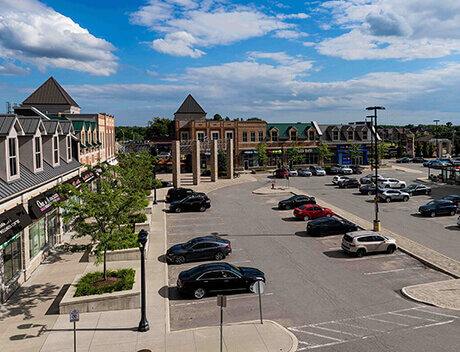 A view of a shopping plaza with parked cars, storefronts on the left, and partially cloudy skies above—a perfect spot for a Toronto Design Agency to gather inspiration for their next project. Conte Studios