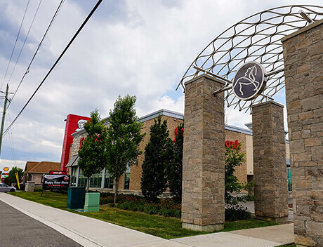 Street view of a building with a stone archway featuring a horse emblem, reminiscent of the creativity at Conte Studios. The structure boasts red and beige accents, surrounded by trees and a sidewalk in Toronto, where design agencies thrive amidst urban charm. Conte Studios