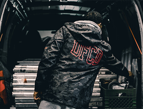 A person in a camo jacket with red letters is meticulously arranging items in the back of a van. It's almost as if they're organizing brand elements for a dynamic Toronto web design agency project. Conte Studios