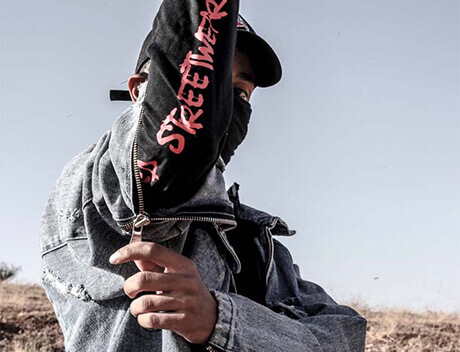 A person in a denim jacket and cap stands outdoors, raising an arm emblazoned with "Streetwear," embodying the urban flair celebrated by Toronto Design Agency. Conte Studios