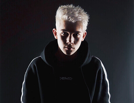 A person with short, light hair in a dark hoodie stands against a black background, partially illuminated, embodying the creative essence of a Toronto-based content creation agency. Conte Studios