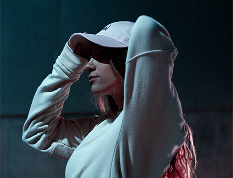 A person in a white hoodie and cap stands in the low light, tilting their head slightly as they adjust the cap. The scene captures a moment that embodies the creative spirit found at Conte Studios, a leading content creation agency in Toronto. Conte Studios