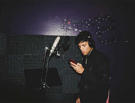 A person wearing headphones stands in a recording booth, looking at a phone. Musical notes are visible on the wall, reminiscent of the creative spirit you'd find at a Toronto design agency. Conte Studios