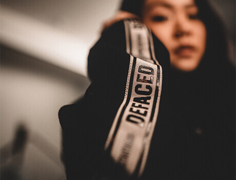 A person donning a black hoodie labeled "DEFACED" on the sleeve, partially blurred, reminiscent of streetwear styled by a Toronto design agency. Conte Studios