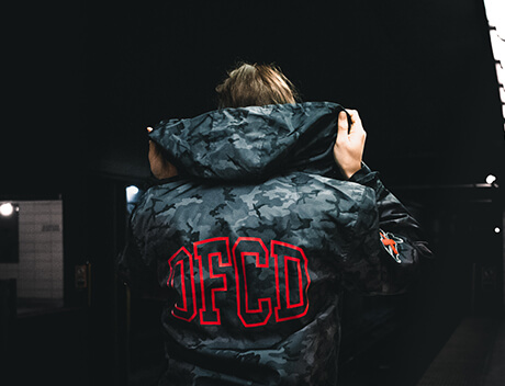 In a dimly lit space, a person clad in a camo jacket emblazoned with bold red "OFCD" lettering adjusts the hood. This intriguing scene unfolds like a creative project from a Toronto Design Agency, where every detail tells its own story. Conte Studios