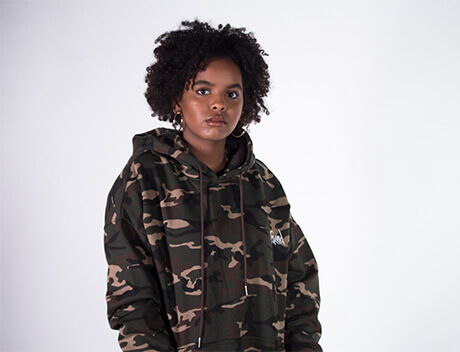 A person wearing a camouflage hoodie stands against a white background, poised like they're ready for a creative campaign from a leading Content Creation Agency in Toronto. Conte Studios