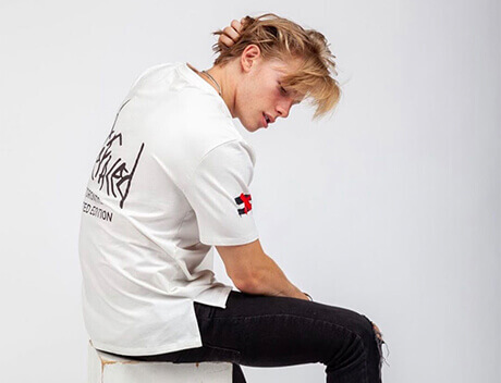 A person sits on a white block, looking back, wearing a white shirt with black text and black pants against a plain white background, embodying the sleek aesthetic of a Toronto Design Agency. Conte Studios