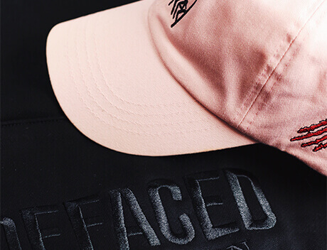 A pink baseball cap with embroidered logos rests on a black surface, the raised text "DEFACED" showcasing the edgy creativity of Conte Studios, a renowned brand design agency in Toronto. Conte Studios