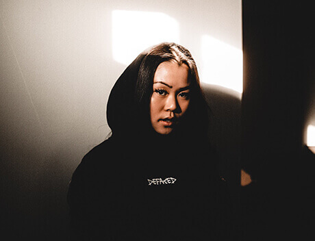 A person wearing a hoodie stands against a wall adorned with light patterns, embodying the creative spirit of a Content Creation Agency in Toronto. Conte Studios