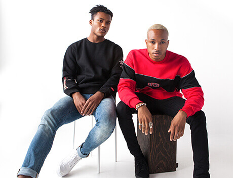 Two people sitting against a white background; one in a black sweater and jeans, the other in a red and black sweater and black pants. Capturing the essence of collaboration, Conte Studios in Toronto brings vibrant storytelling to life through stunning imagery. Conte Studios