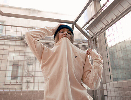 A person in a beige shirt, partially covering their face with a beanie, stands thoughtfully by a metal fence, embodying the creative spirit of Brand Design Agency Toronto. Conte Studios