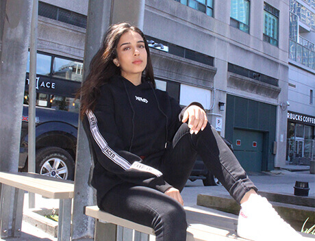 A woman in a black tracksuit sits on a bench in an urban area, where the sleek architecture mirrors the innovation found in a leading Brand Design Agency Toronto. Buildings and a parked car stand quietly in the background. Conte Studios