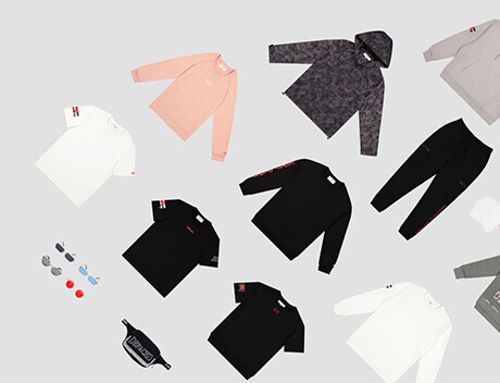 A flat lay of various clothing items on a light grey background, featuring hoodies, T-shirts, pants, a fanny pack, and small accessories like sunglasses and socks in neutral and dark colors. Ideal for content creation by a Toronto Design Agency looking to inspire stylish ensembles. Conte Studios