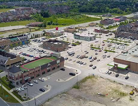 Aerial view of a suburban commercial area, featuring the bustling hub of Conte Studios—an acclaimed Toronto Design Agency. Surrounding parking lots and buildings blend seamlessly into the adjacent residential houses, capturing the vibrant essence of content creation in the city. Conte Studios