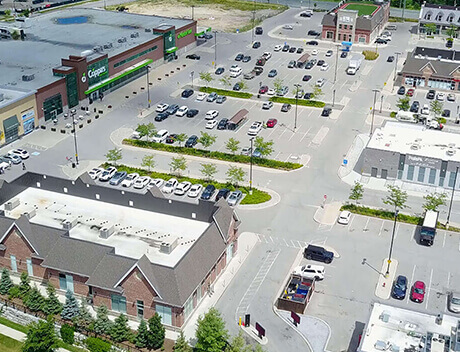 An aerial view of a large parking lot with scattered cars, bordered by commercial buildings and green spaces, embodies the structured creativity akin to a Toronto Design Agency. Conte Studios