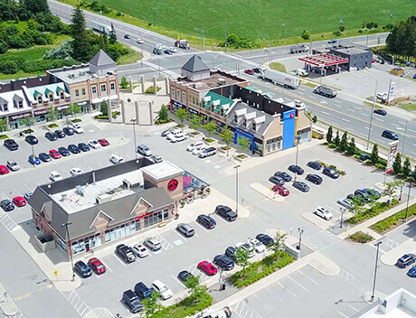 Aerial view of a bustling shopping center featuring parked cars, diverse retail buildings, and surrounding roads, captured with the keen eye of Conte Studios, a leading Toronto design agency. Conte Studios