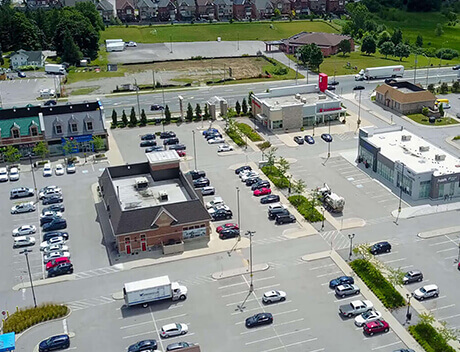 Aerial view of a shopping plaza in Toronto, bustling with cars and vibrant activity. Amidst the buildings, a few trees stand gracefully, while the road and grassy areas stretch into the background. Nearby, a prominent Brand Design Agency gives this locale its unique flair. Conte Studios